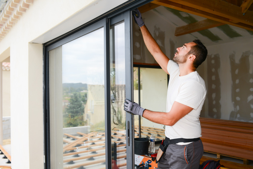 A man wearing gloves installing a large glass door or window on a new home