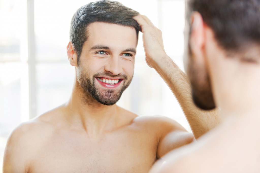 man touching his hair with hand and smiling while standing in front of the mirror