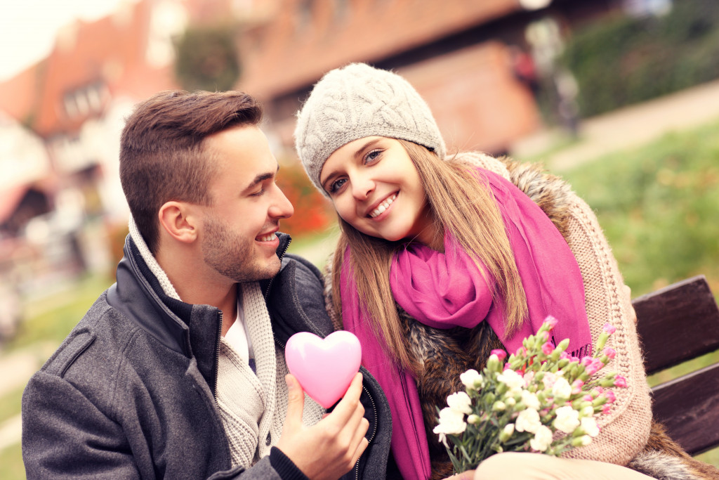 A picture of a couple in the park with flowers and heart