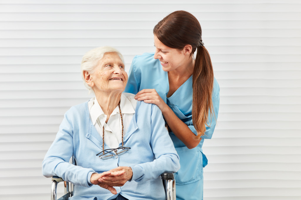 Nurse holding the shoulders of a senior woman sitting on a wheelchair.