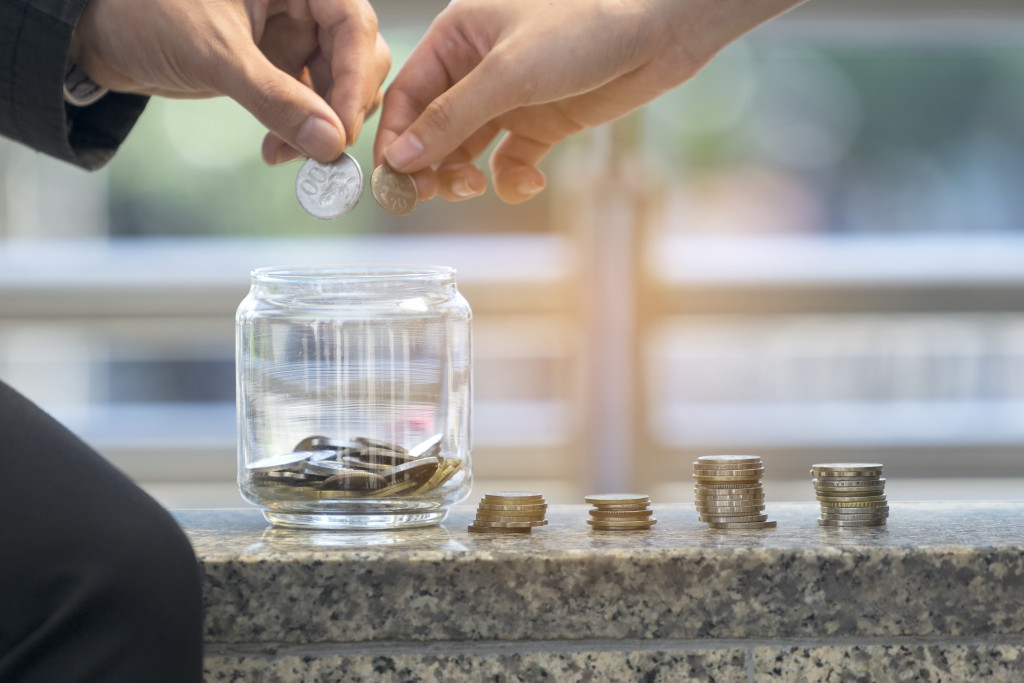 Two people putting coins into a jar with four other coins stacks beside it