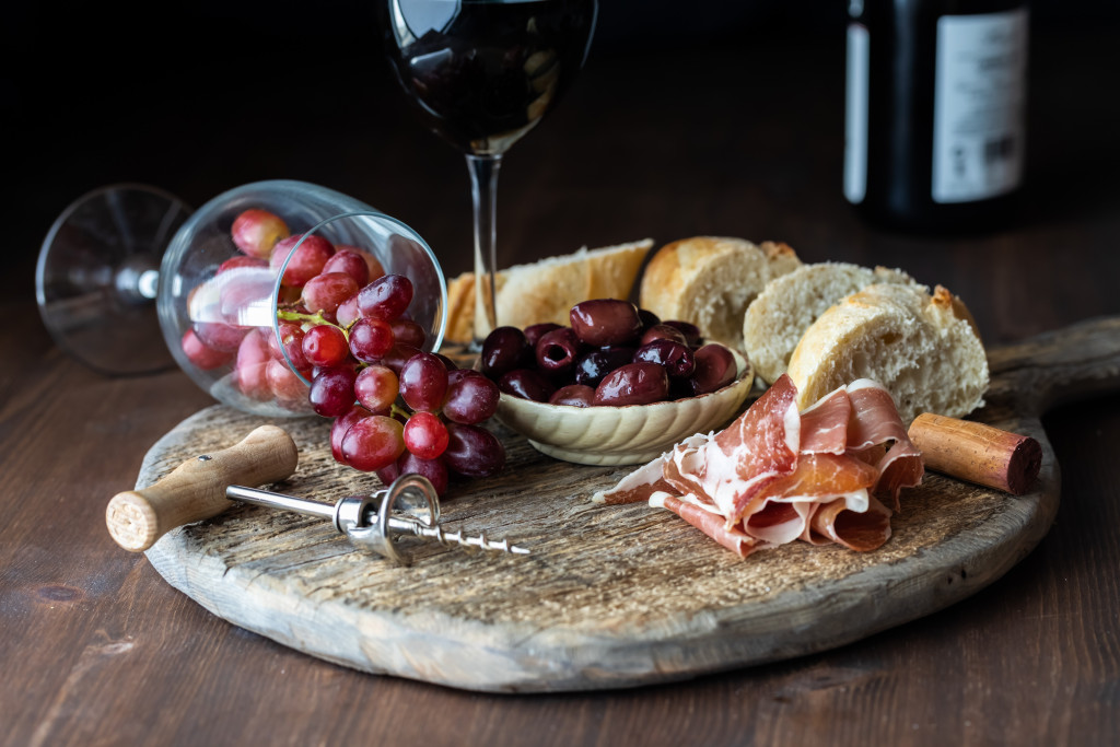 A \charcuterie board with grapes, wine, bread, meats, and olives