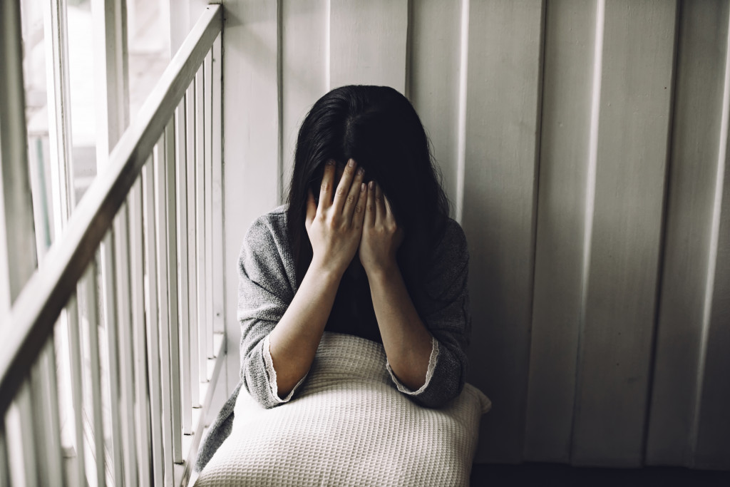 young woman sitting the corner covering her face