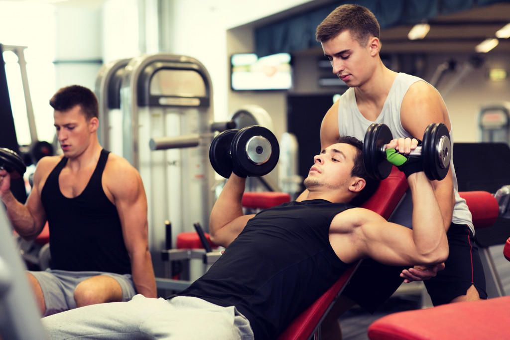 Young man lifting weights at a gym with an instructor guiding him.