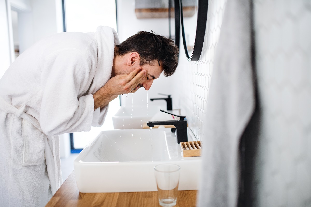 man in bathrobe washing his face