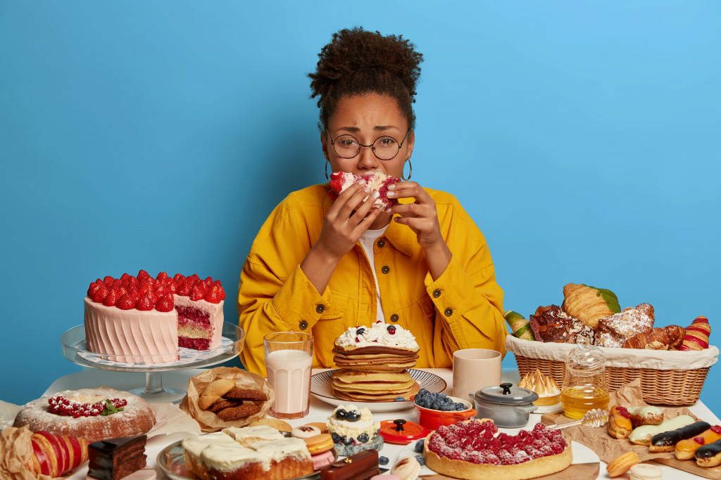 woman with various desserts on table overeating herself
