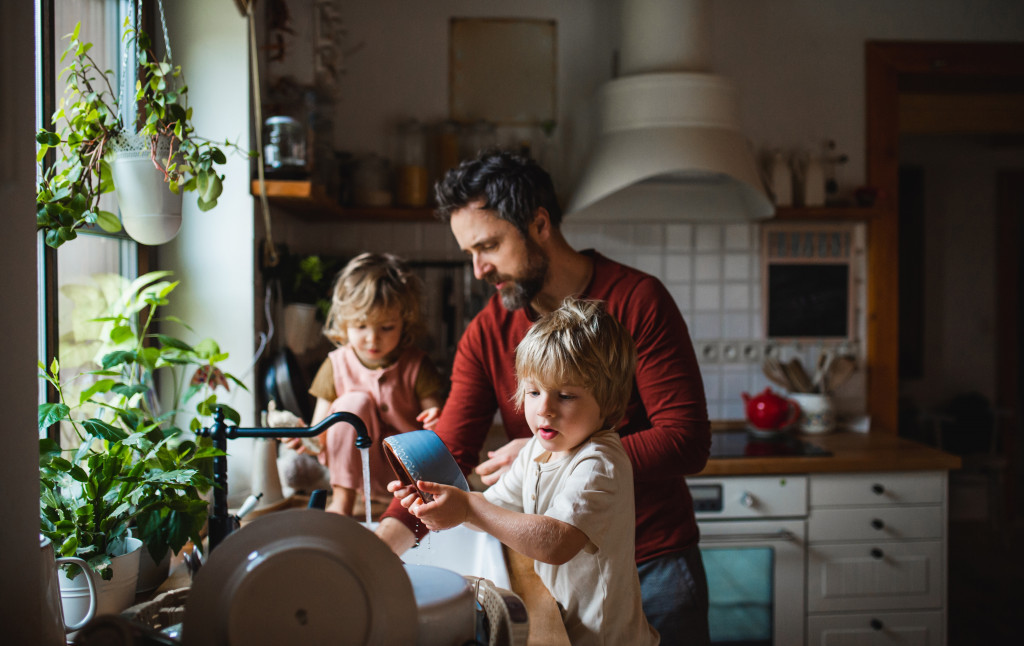 father teaching children to wash dishes