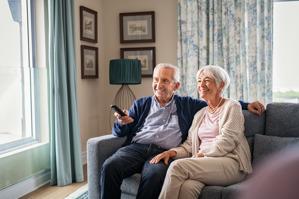Elderly couple watching television while sitting on a sofa at home.